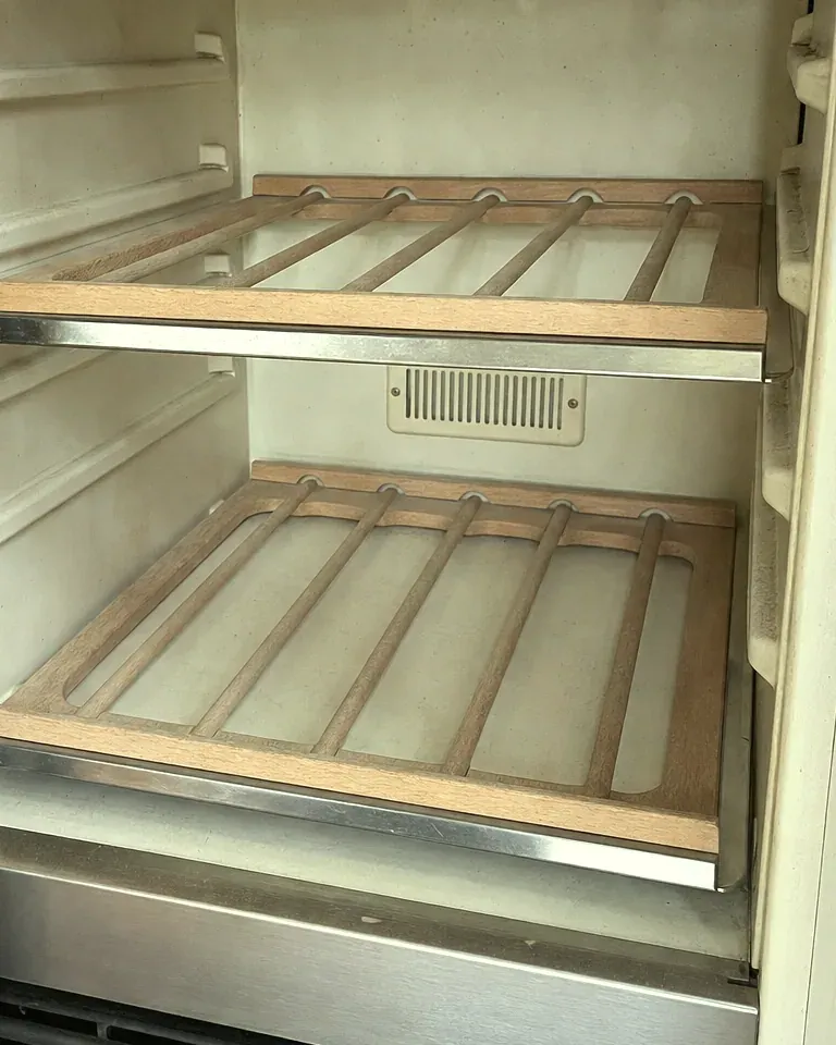 Refrigerator interior with two wood-framed slatted shelves and a small vent on the back wall.